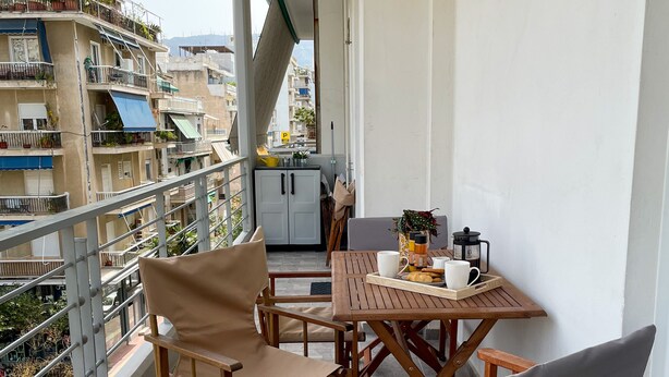 A balcony with a table and chairs, a view of the city, and a building with balconies.