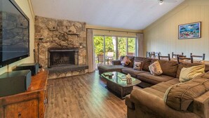 A living room with a stone fireplace, a large flat-screen TV, a sofa, and a coffee table. - Brockway Shores Condo in Kings Beach -Lakeview (Kings Beach)