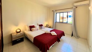 Une chambre d’hôtel comprenant un lit, deux tables de chevet, une fenêtre avec des rideaux et un climatiseur fixé au mur.