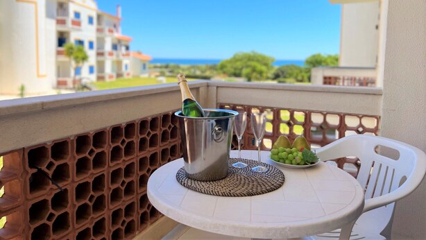 Un balcon avec une table dressée pour deux personnes, un seau en métal contenant une bouteille et une assiette de raisins.