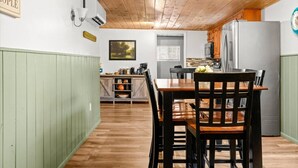 Un comedor con una mesa y sillas de madera, una cocina al fondo y una pared pintada de verde.