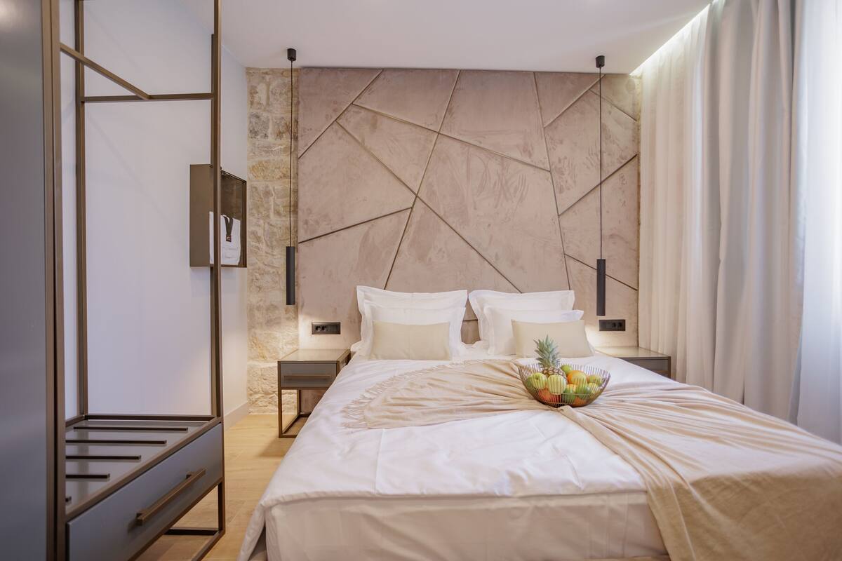 A modern hotel room with a large bed, a nightstand, a wall-mounted TV, and a decorative wall panel.