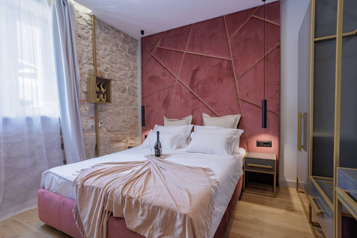 A bedroom with a stone wall, a bed with white linens, a bedside table with a bottle, and a nightstand.