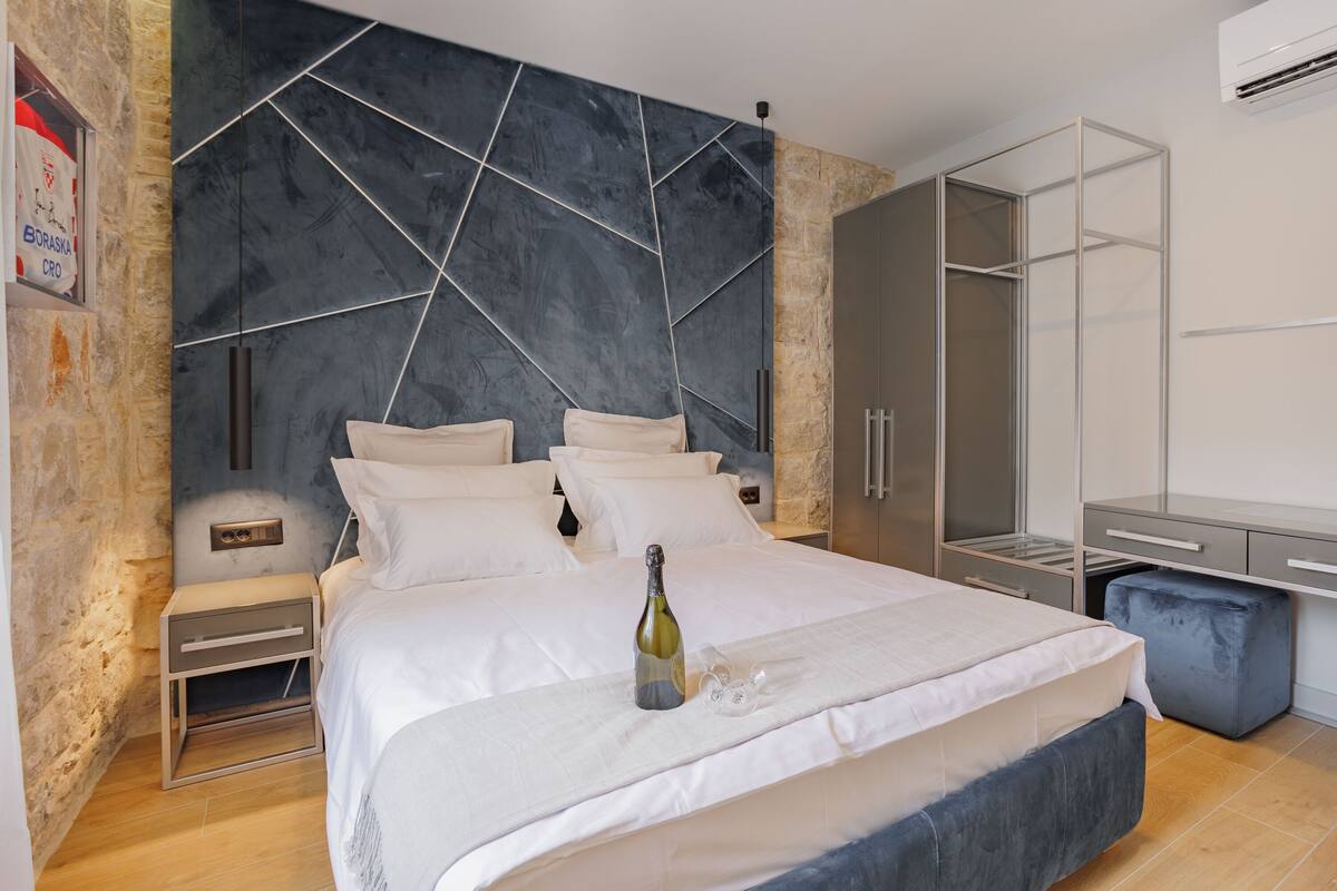 A modern bedroom with a large bed, a nightstand, a wardrobe, and a minibar.