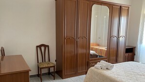 Una camera da letto con un'armadietto in legno, una sedia, un letto con copriletto e un tavolino.