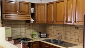Una cucina con mobili in legno, schienale piastrellato, piano cottura, lavello e lampadario.