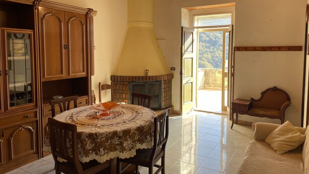 Zona pranzo con tavolo rotondo, sedie e camino. In zona soggiorno, divano e poltrona.