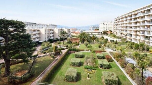Un hotel con varios pisos, un jardín bien cuidado con diversas plantas y árboles, y una vista despejada del entorno.