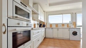 Una cocina moderna con armarios blancos, horno empotrado, lavavajillas y lavadora.