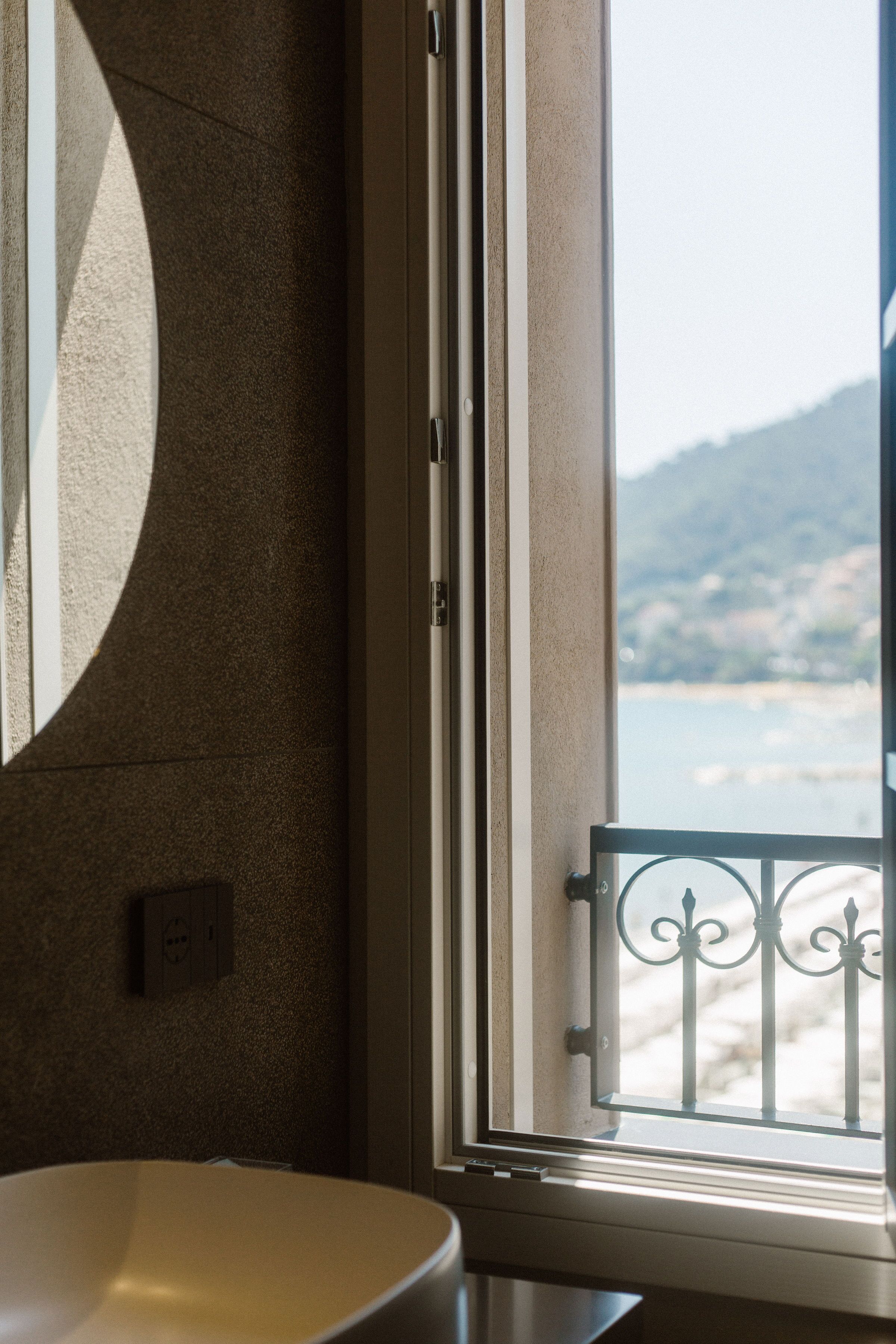 Une salle de bain avec un lavabo rond, un miroir et une fenêtre donnant sur une plage et des montagnes.