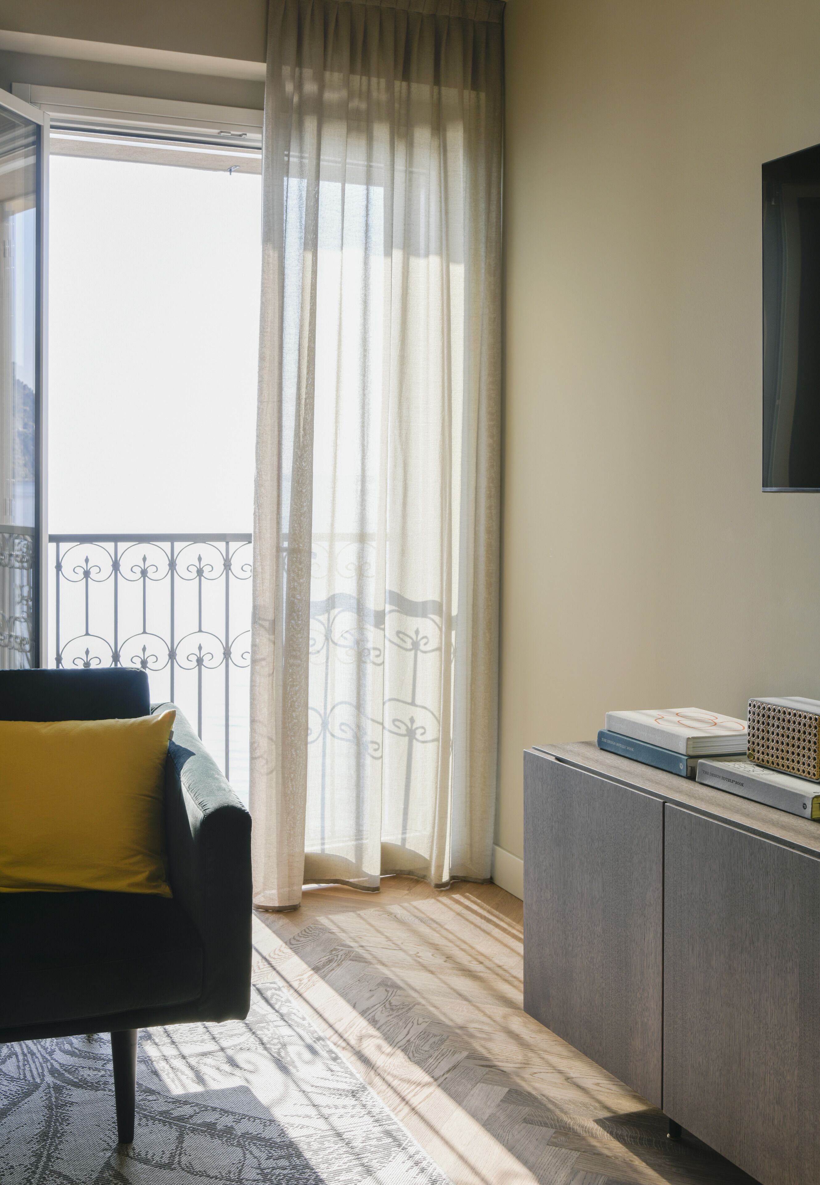 A room with a sofa, a cabinet, and a view through a window with curtains.
