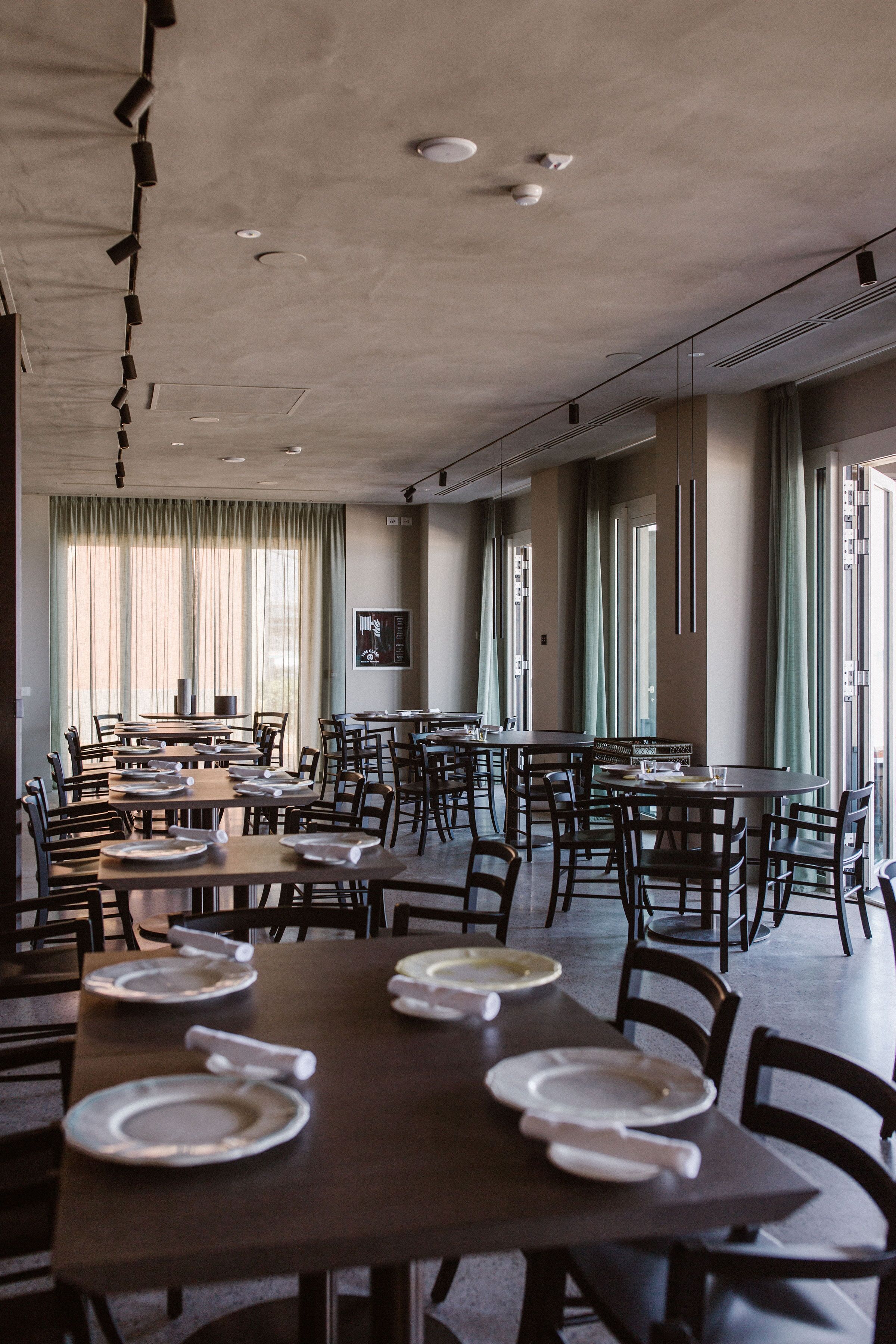 A spacious dining area with multiple tables and chairs, large windows with curtains, and a modern ceiling design.