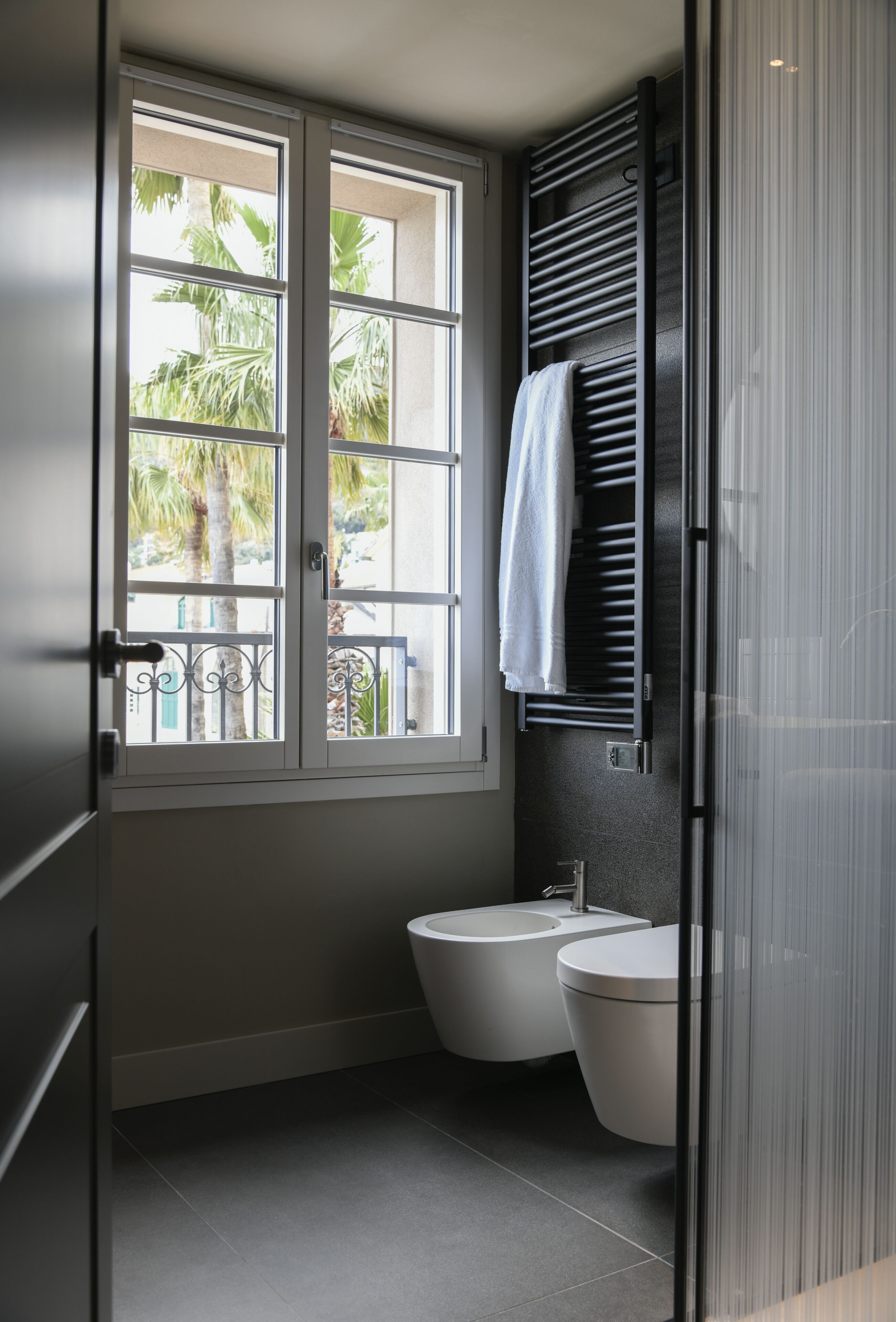 Un baño moderno con ventana, dos inodoros y una toalla colgada en un perchero.