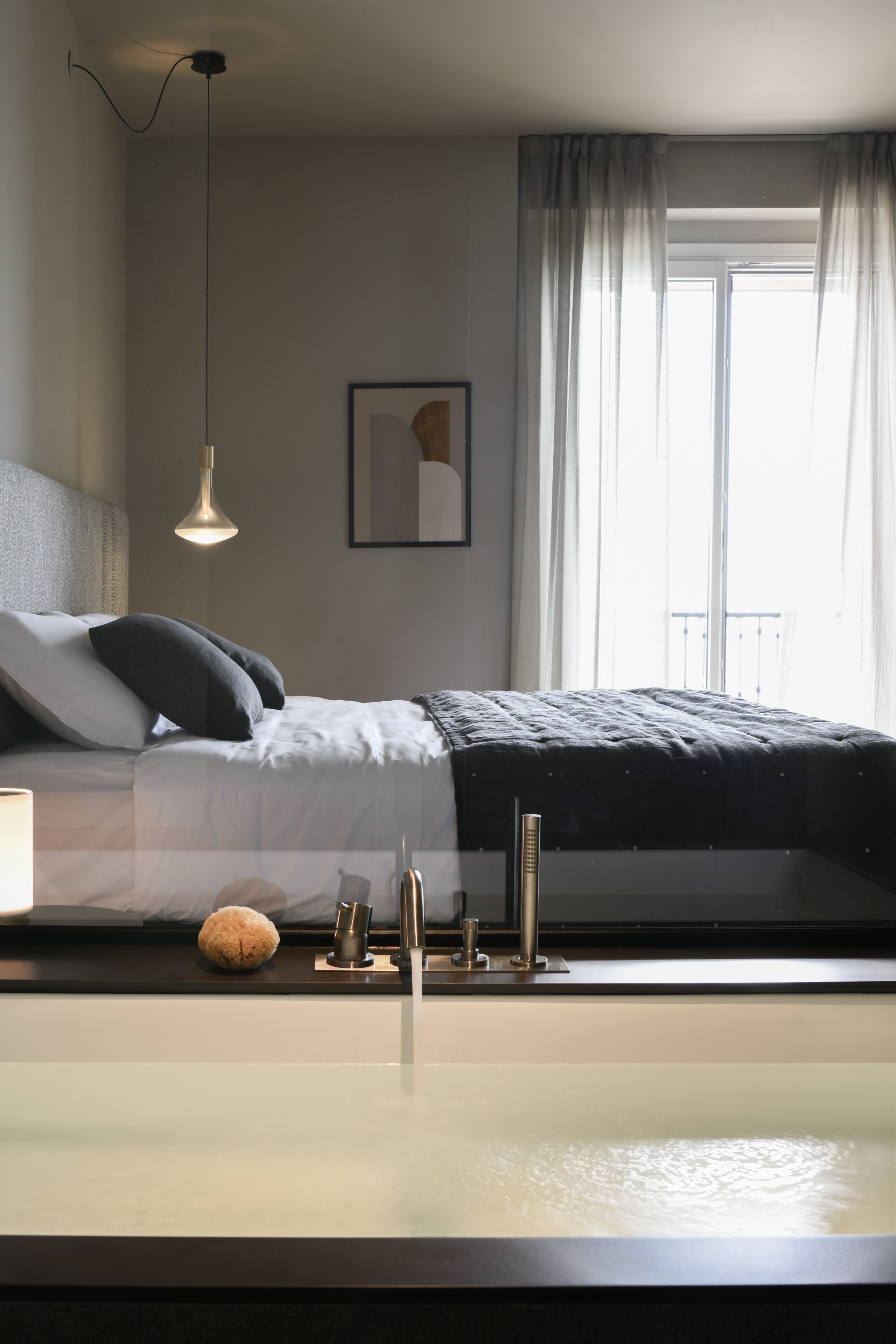 A modern bedroom with a bed, bedside table, and a large window with curtains.