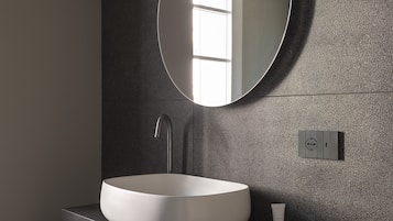 A modern bathroom with a round mirror, a white sink, and a shelf with towels.