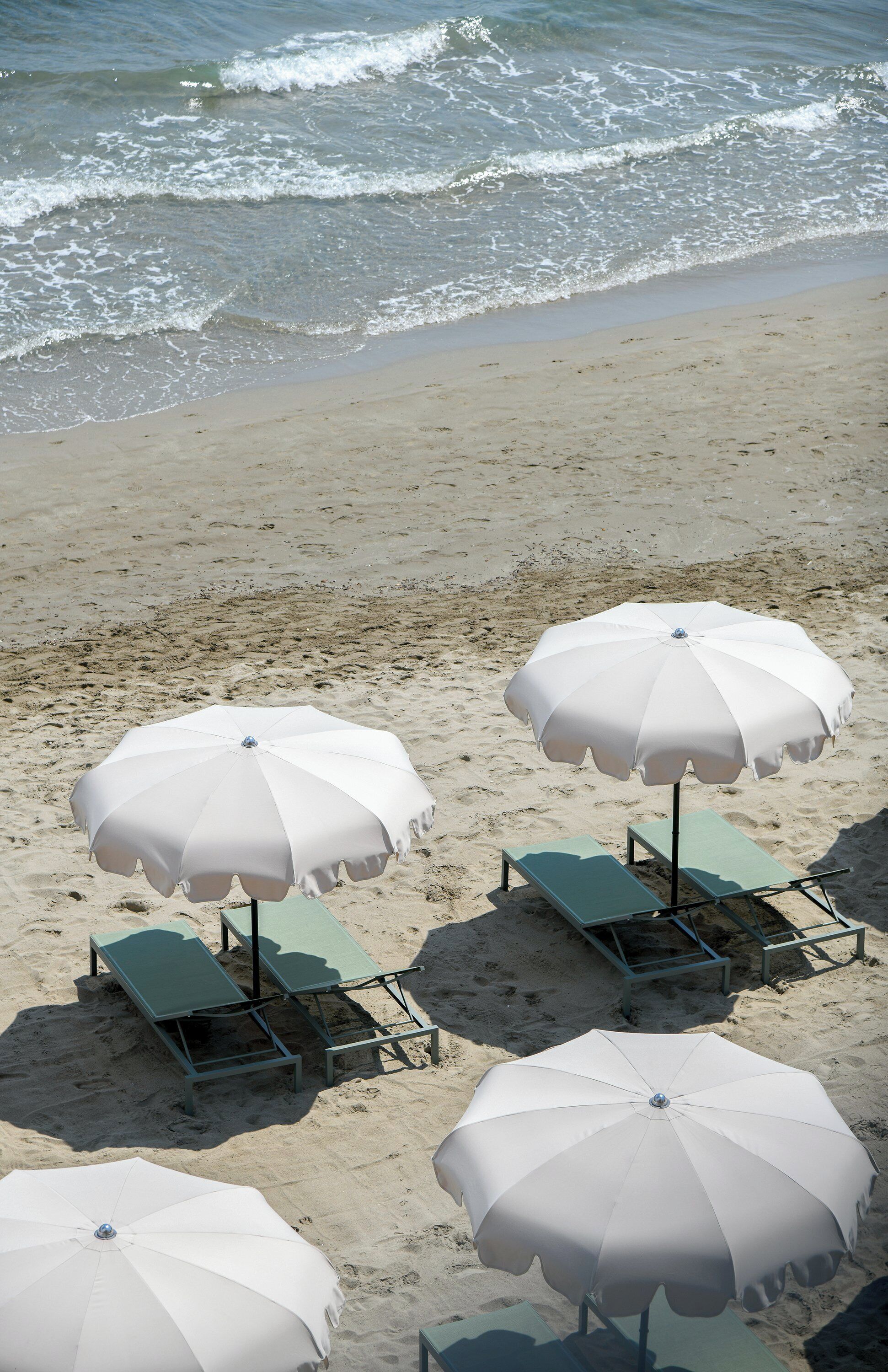 Una playa con sombrillas blancas y sillas de descanso verdes.