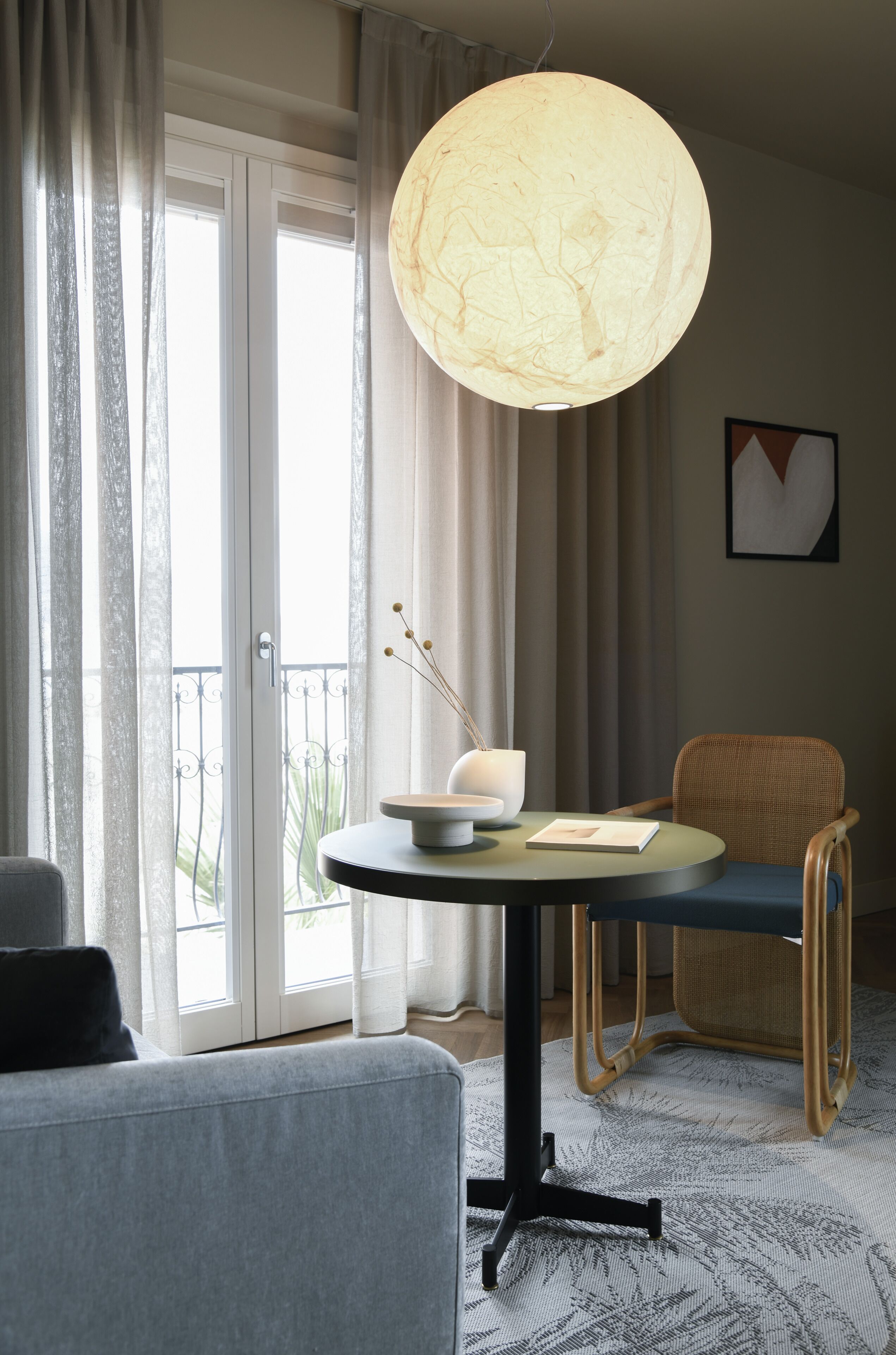 A room with a round table, a chair, a lamp, and a view through a door.