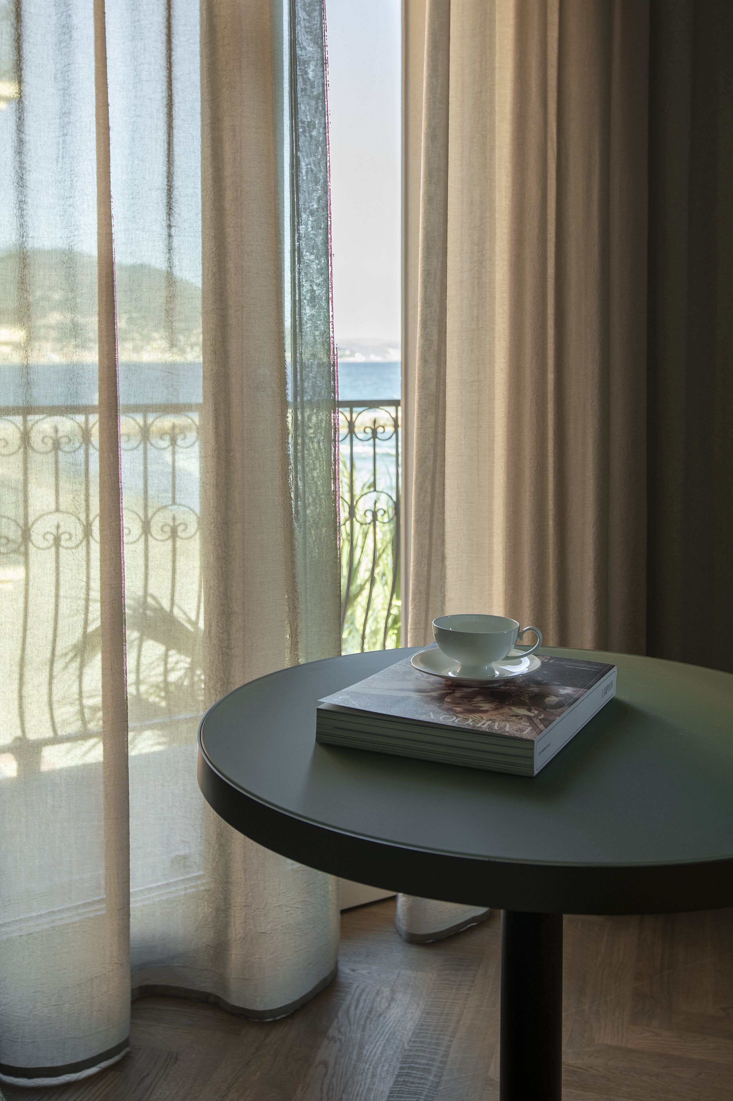 A table with a cup and a book, near a window with curtains.