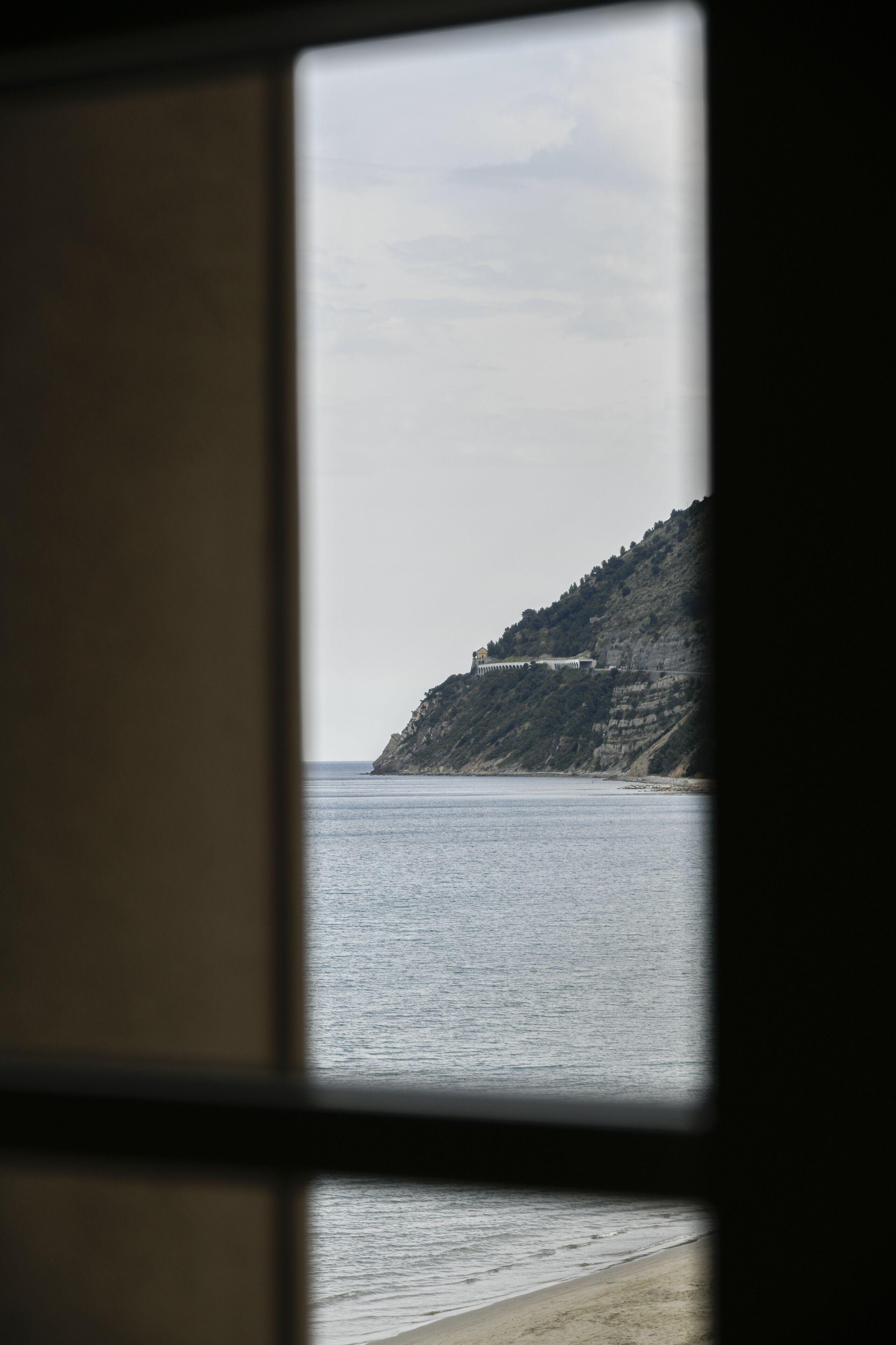 A view through a window of a coastal landscape with a building on a cliff.