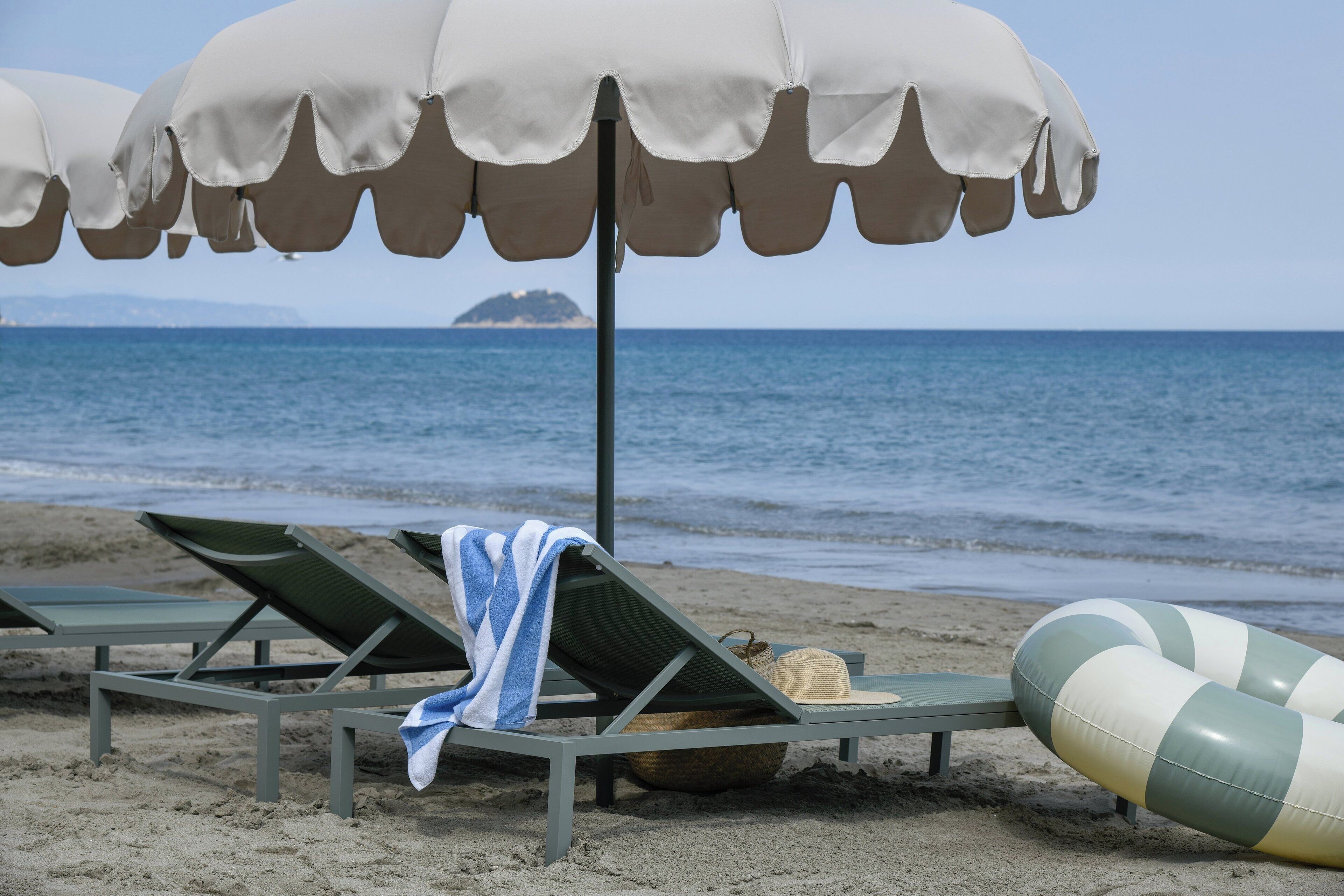 A beach with lounge chairs, umbrellas, and a beach ball.