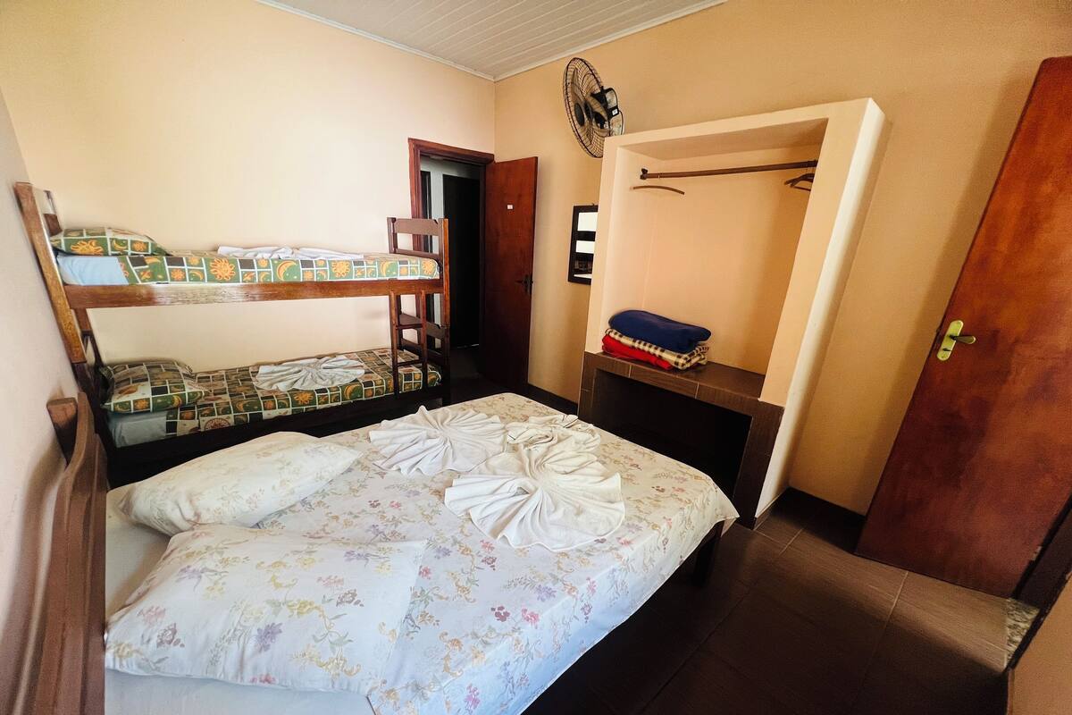 Una habitación con dos literas, una silla de madera, una mesita con un ventilador y una puerta.