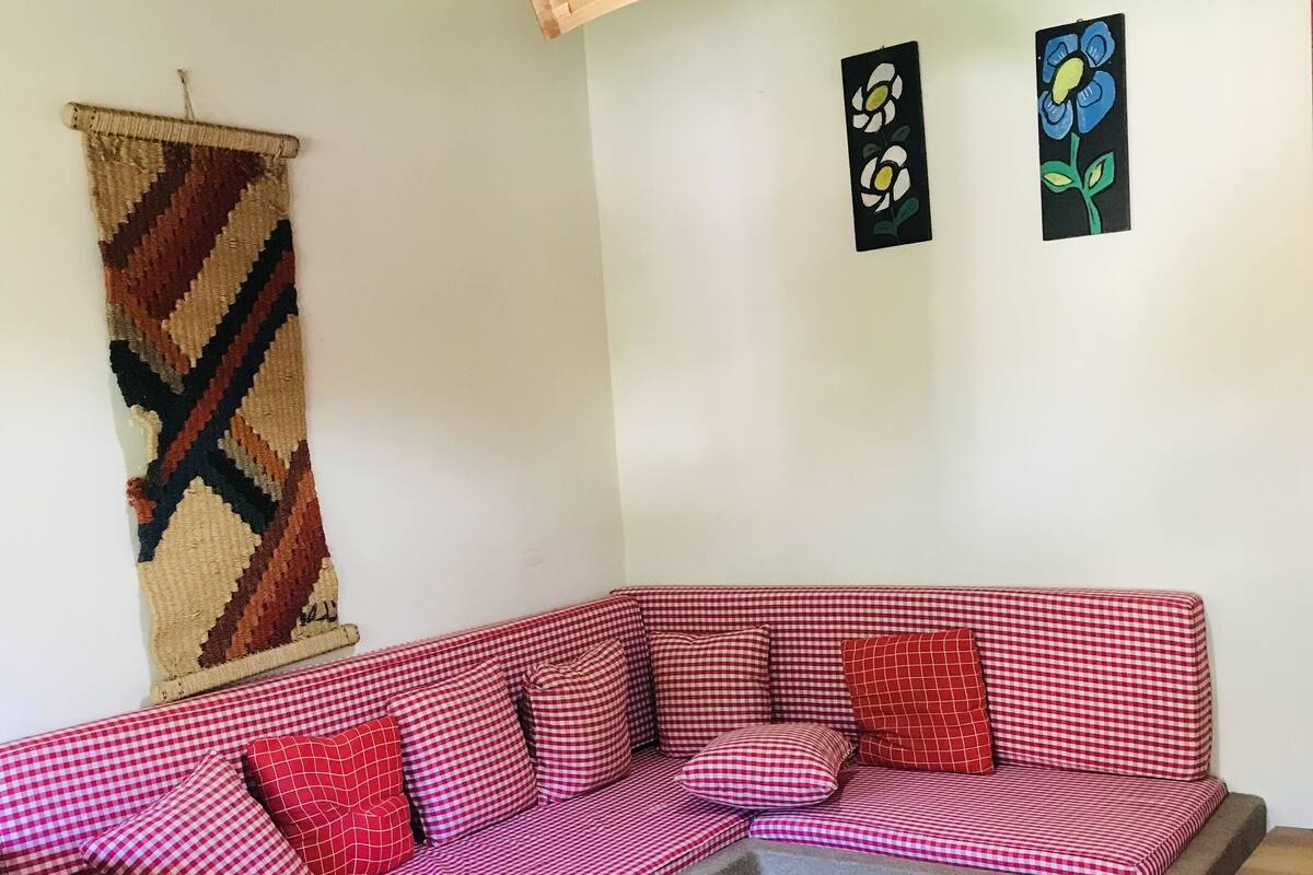 Una habitación acogedora con un sofá a cuadros, un tapiz tejido y dos cuadros de flores colgados en la pared.