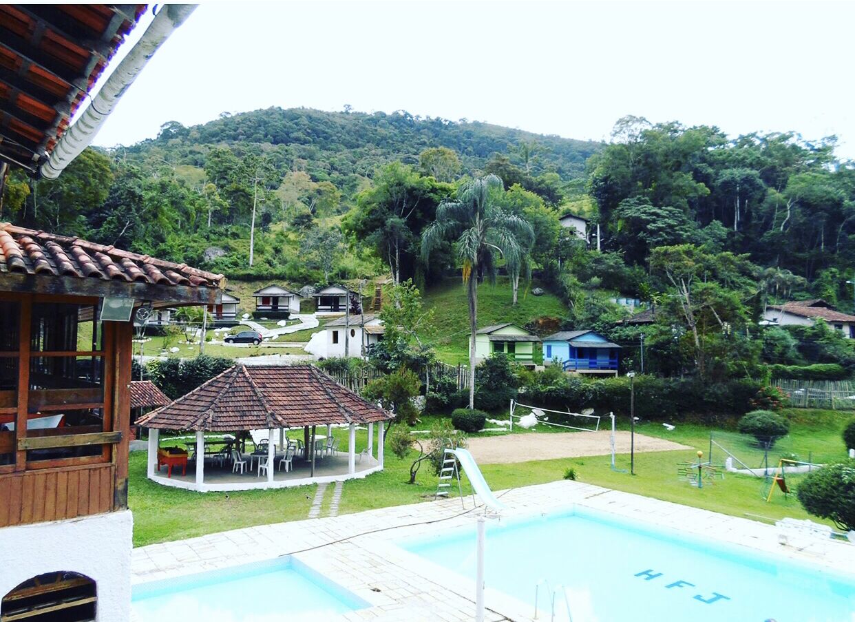 Una piscina con un pabellón y zona de descanso, rodeada de abundante vegetación y colinas.