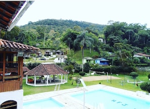 A swimming pool with a gazebo and lounge area, surrounded by lush greenery and hills. - Hotel fazenda jequitibá (Nova Friburgo)