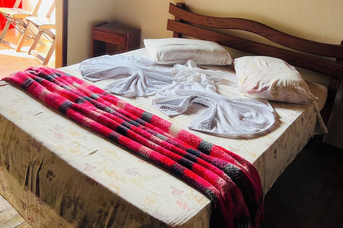 Una cama bien hecha con una colcha estampada, una manta a rayas rojas y negras y dos almohadas blancas.