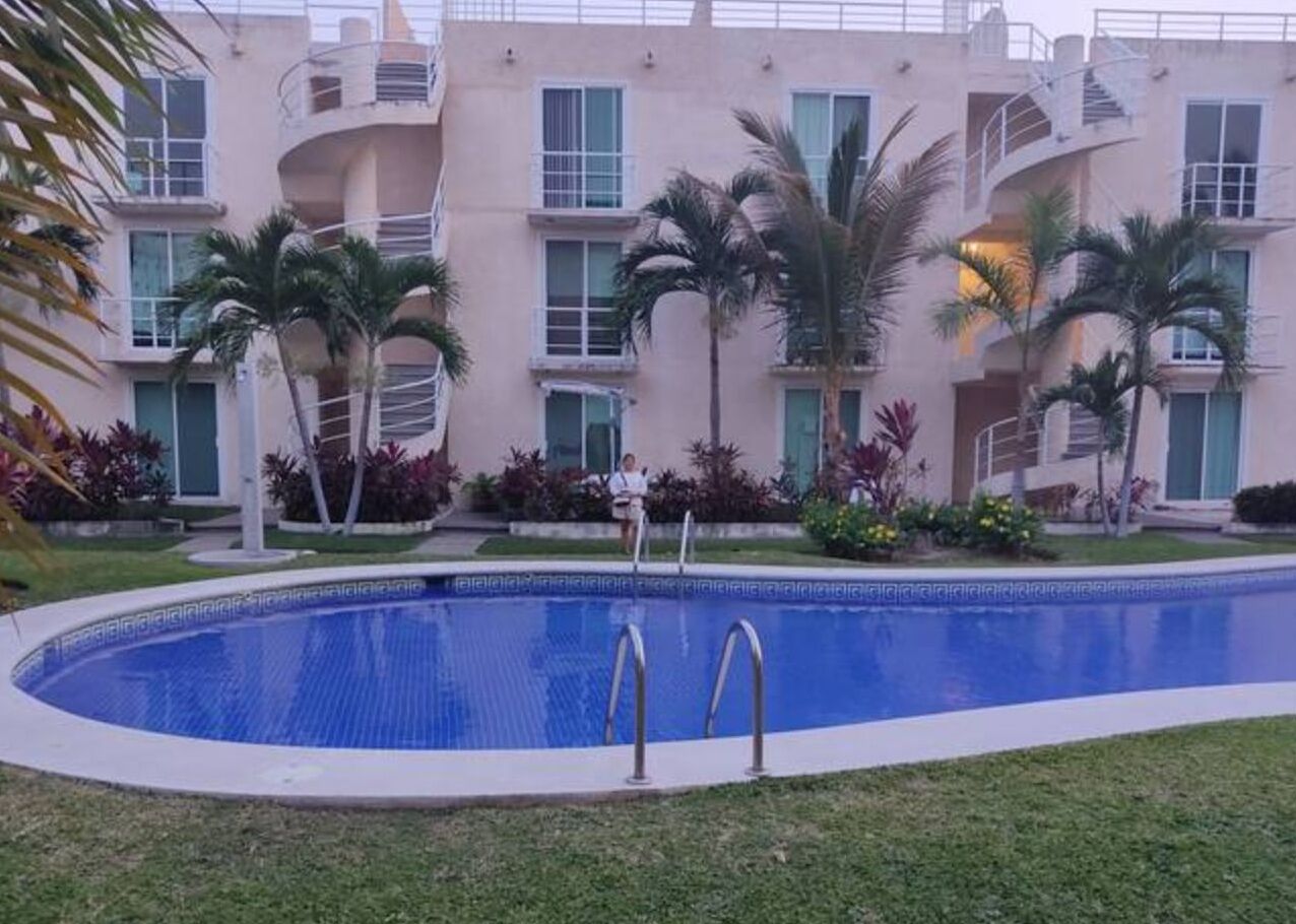 Una piscina con dos escaleras, rodeada por un césped cuidado y palmeras.