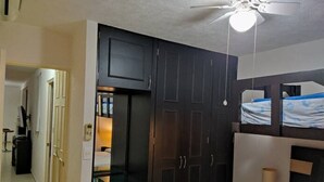 A bedroom with a dark wood wardrobe, a ceiling fan, and a bunk bed with a blue and white striped blanket.