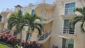 A multi-story hotel with balconies, palm trees, and a pool area.