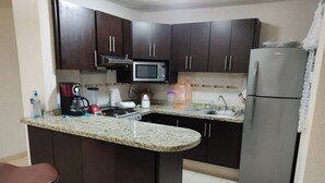 A compact kitchen with dark cabinets, a granite countertop, a microwave, a refrigerator, and a sink.