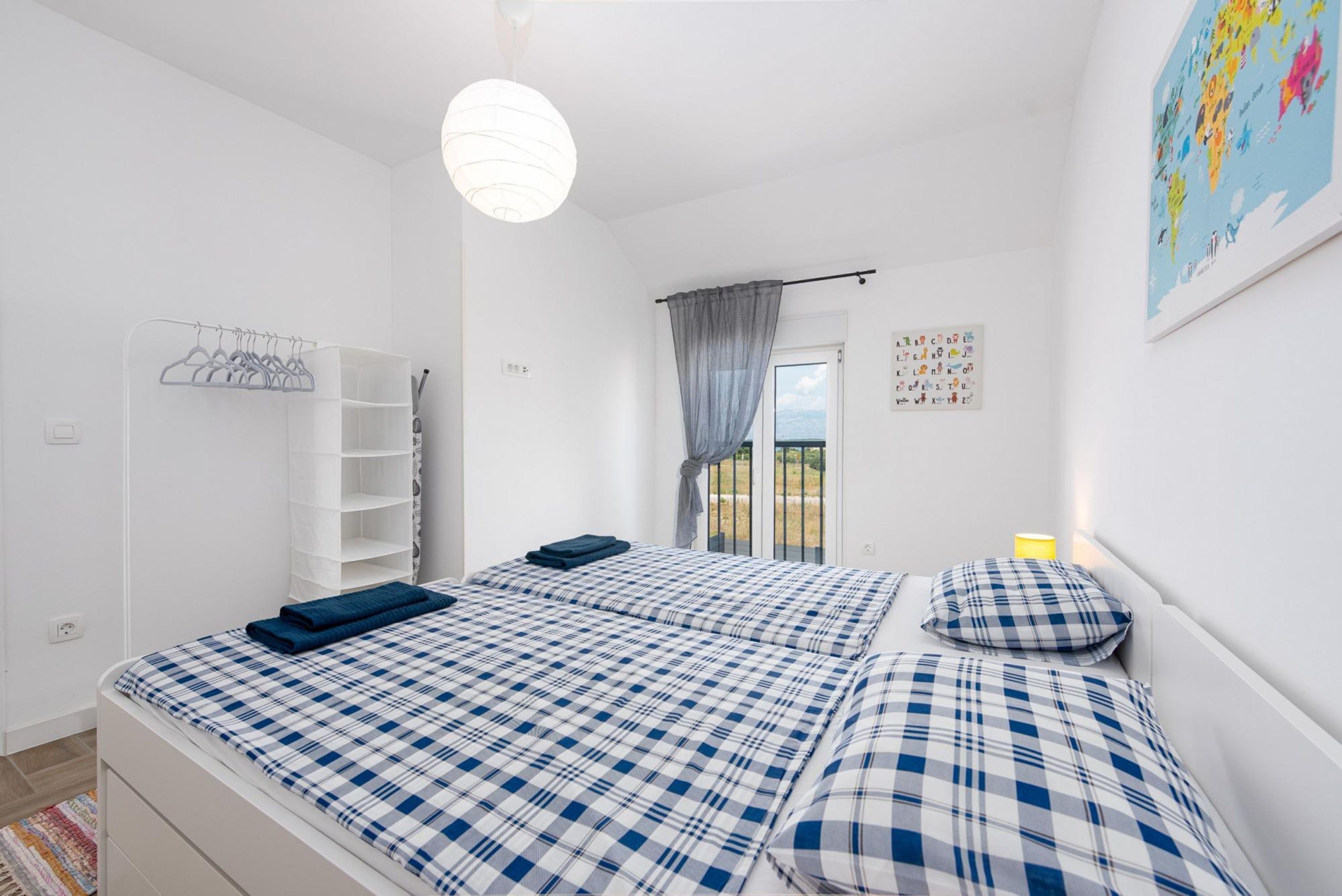 Quarto com cama, guarda-roupa, cabideiro, janela com cortinas e parede com mapa.