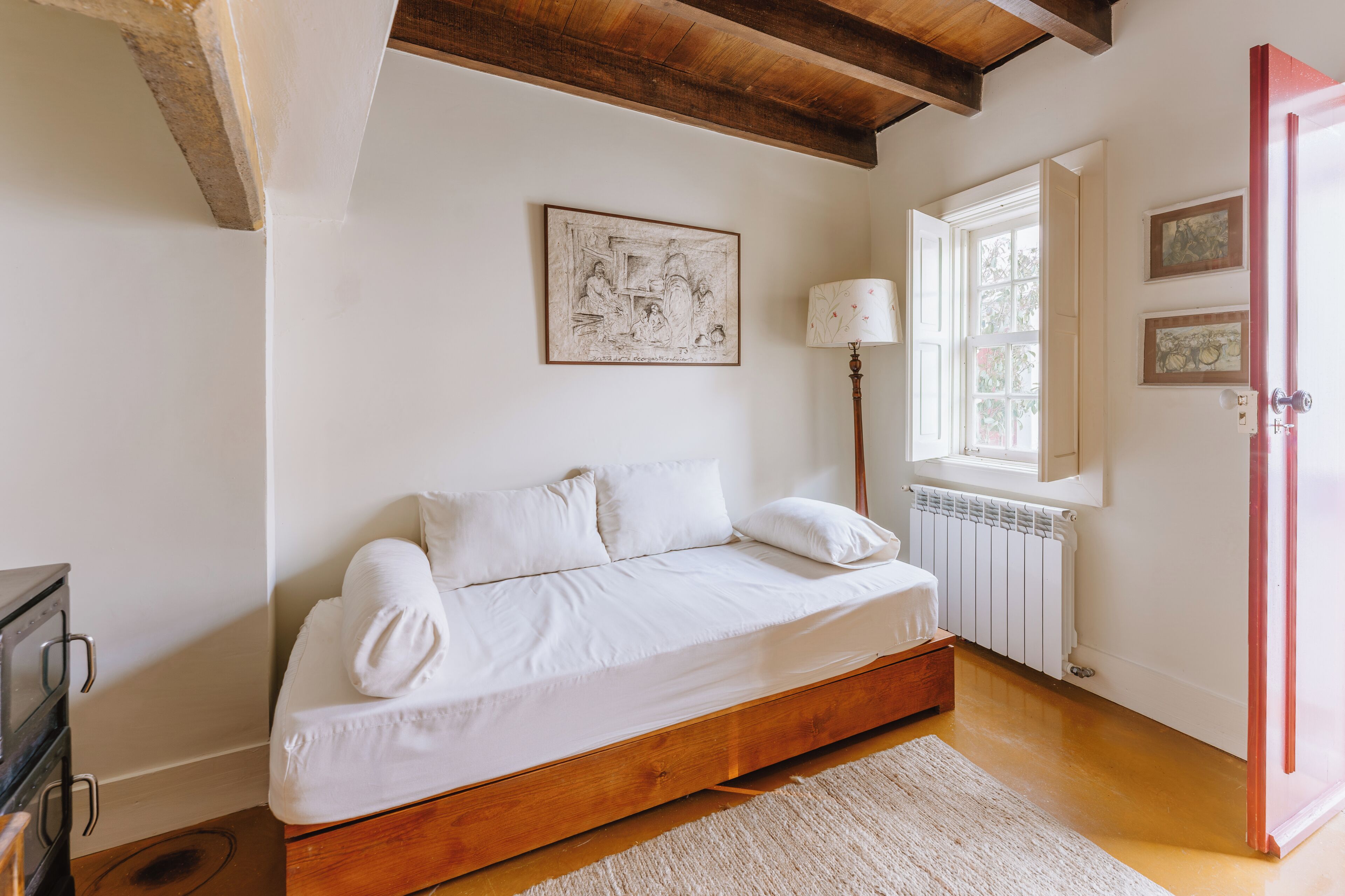 Un dormitorio con cama de madera, un radiador, una ventana con vistas y una puerta.