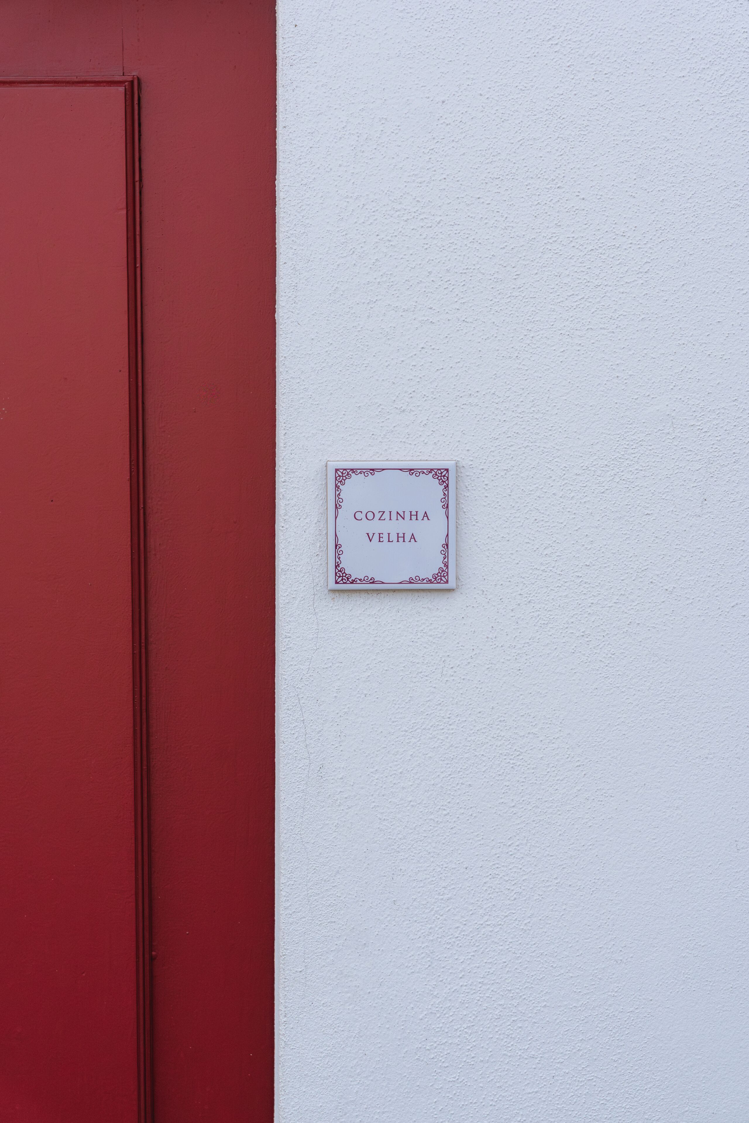 Una porta vermella i una paret blanca amb un rètol que diu 'COZINHA VELHA'.