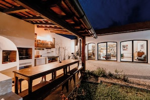 A modern outdoor dining area with a wooden bench and a table, surrounded by a garden with pebbles and plants. - Galricho Heritage House (Murtosa)