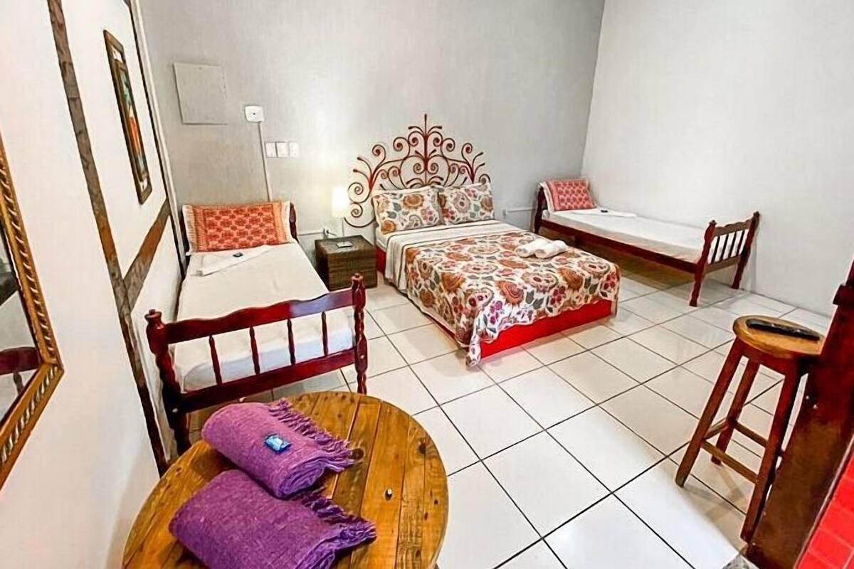 A bedroom with a bed, a chair, a table, and a mirror.