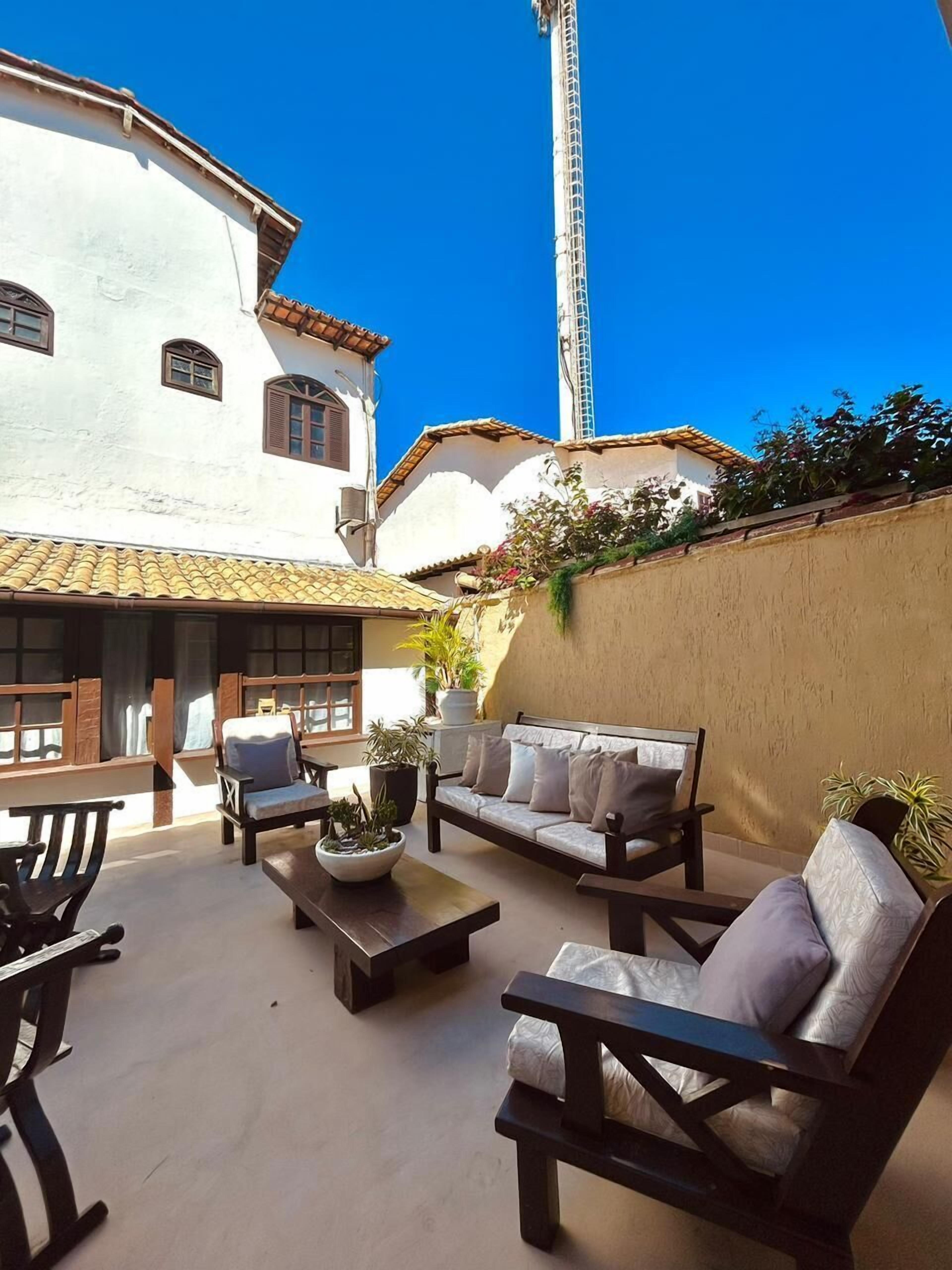 Un patio con un edificio blanco, una torre alta y mobiliario exterior con cojines y una mesa de centro.