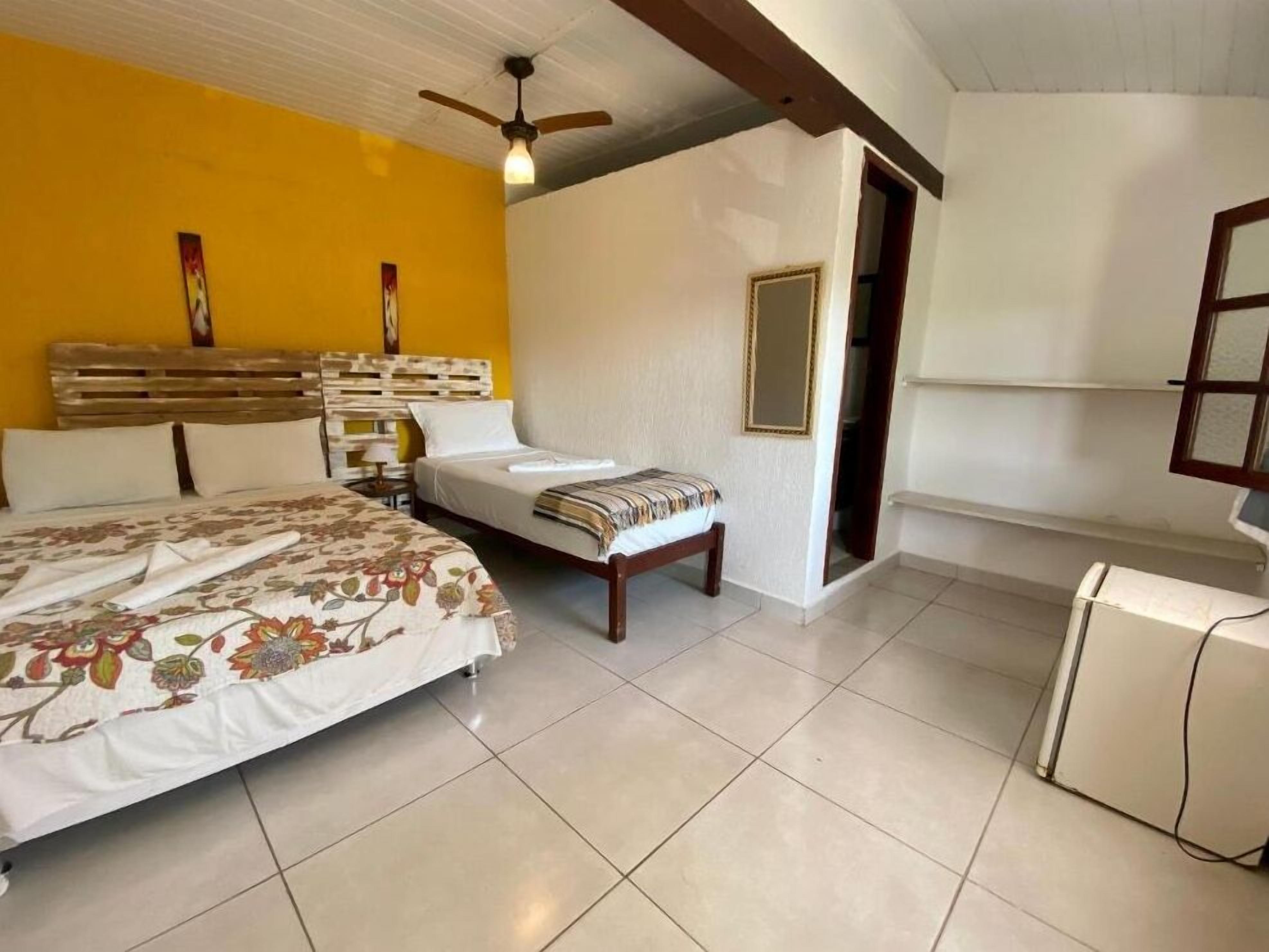 A bedroom with a bed, a bench, a ceiling fan, and a small white cabinet.