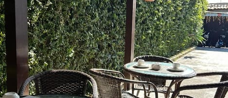 An outdoor seating area with wicker chairs and round glass tables, some with tea sets.