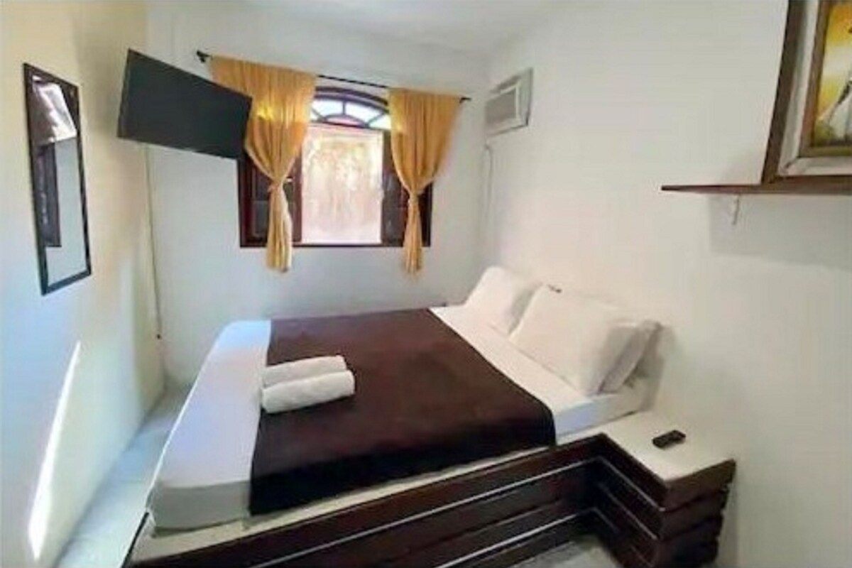 A single bed with a dark headboard, white bedding, and a small bedside table with a lamp.