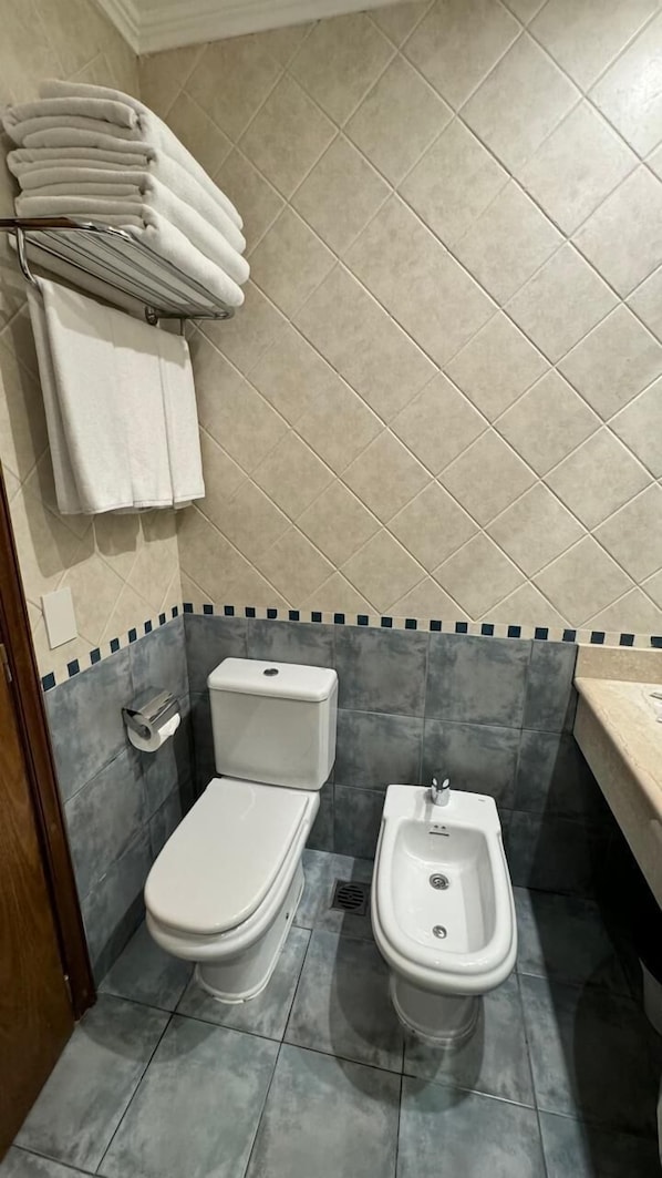 Un baño pequeño con inodoro, bidé y un perchero con toallas dobladas.