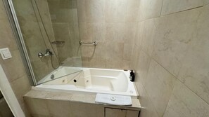 A modern bathroom with a glass-enclosed shower, a white bathtub, and beige tiled walls. - Gardi Hotel & Suites (Buenos Aires)