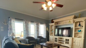 Una sala de estar con un sofá, dos sillones, una mesa de centro, un televisor y un ventilador de techo.