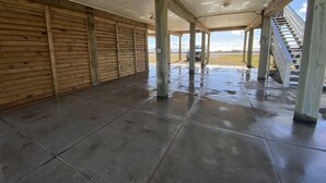 Un espacio al aire libre cubierto, con piso de concreto, paredes de madera y una escalera que conduce a un nivel superior.