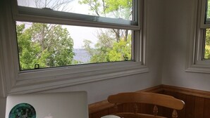 A laptop with a sticker on a table next to a wooden chair, with a window view of trees and a body of water. - Enjoy the Summertime Beaches, Concerts and Events in Prince Edward County! (Prince Edward)