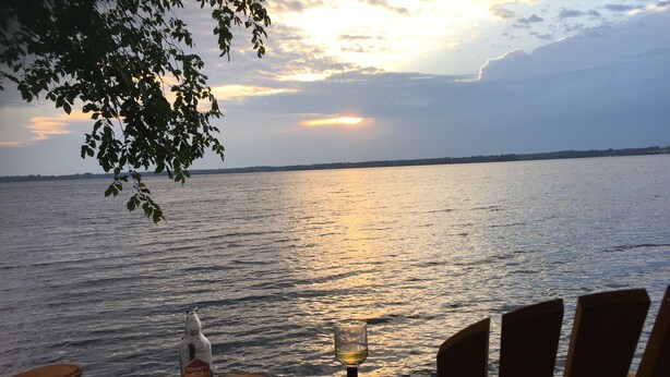 A wooden deck with two chairs facing a body of water at sunset. - Enjoy the Summertime Beaches, Concerts and Events in Prince Edward County! (Prince Edward)