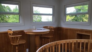 A corner room with a round wooden table, two wooden chairs, and a crib. There are three windows providing views of trees. - Enjoy the Summertime Beaches, Concerts and Events in Prince Edward County! (Prince Edward)