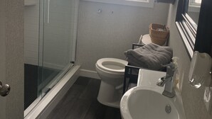 Un baño con cabina de ducha de vidrio, inodoro, lavamanos y ventana.
